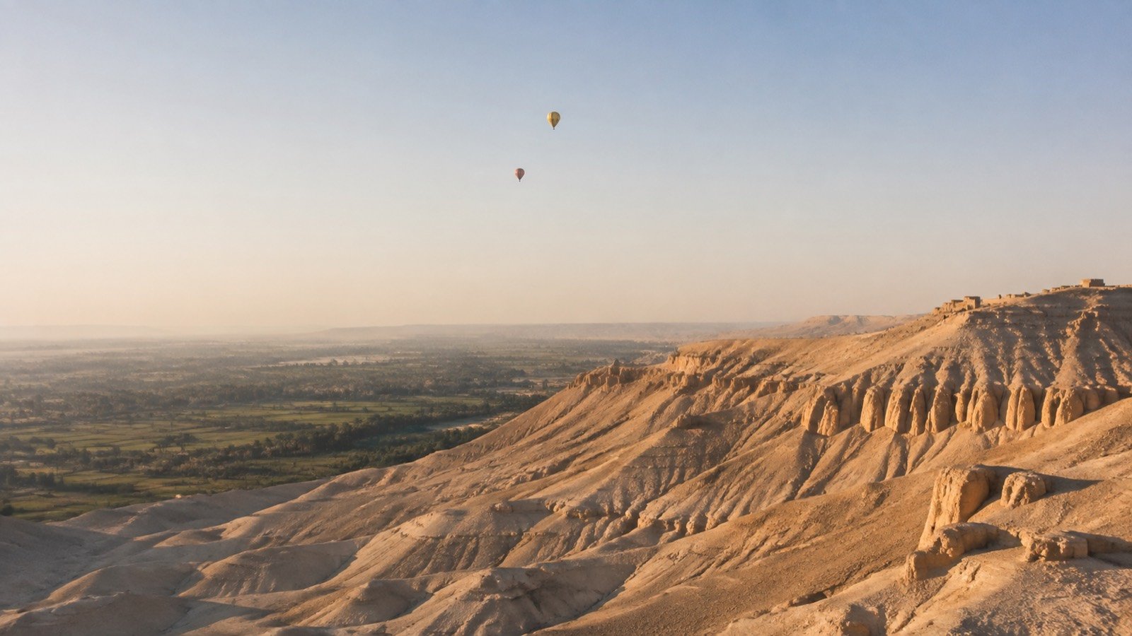 Editorial illustration of morning balloons beyond Luxor’s desert hills